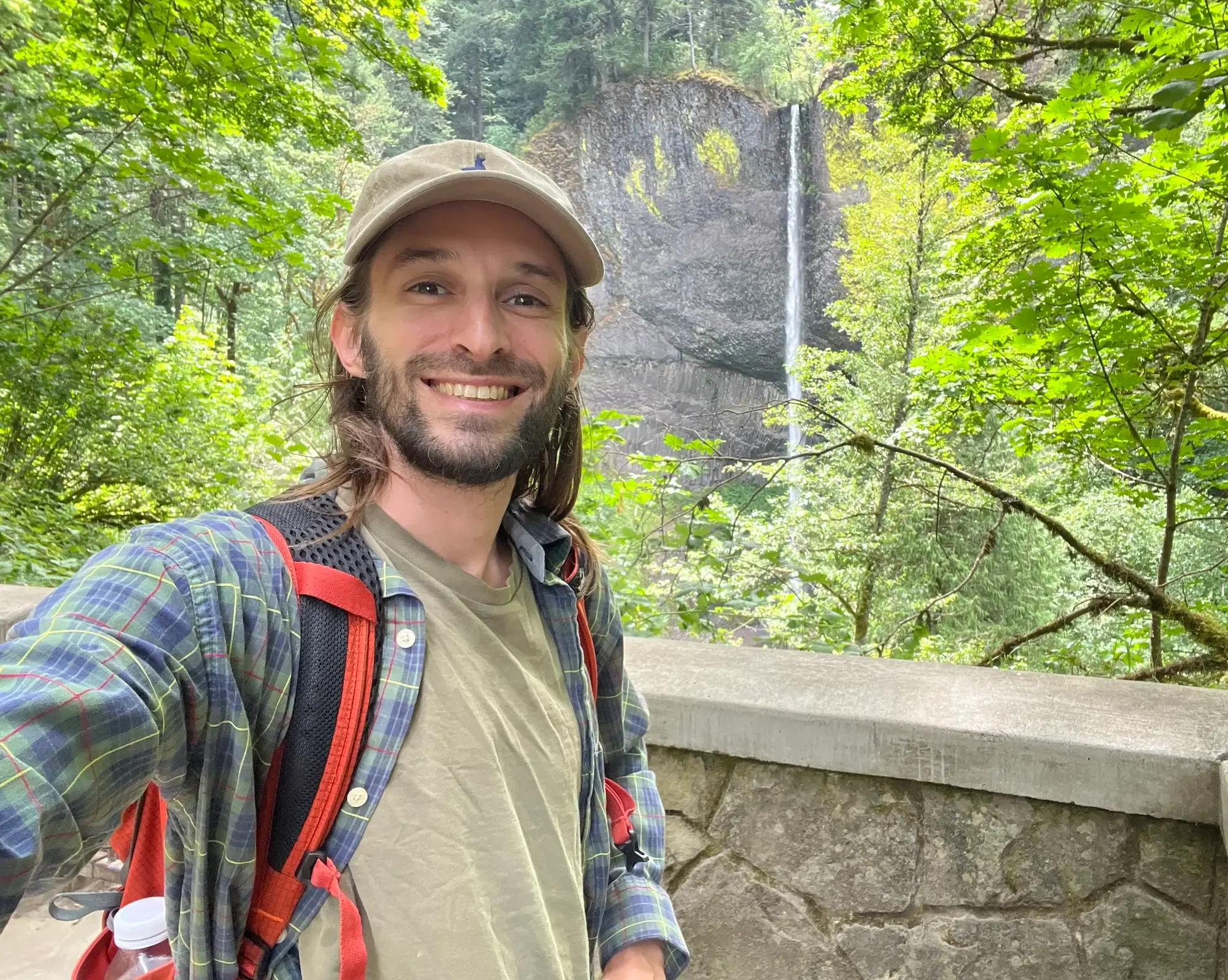 smiling guy with a hat in front of a waterfall